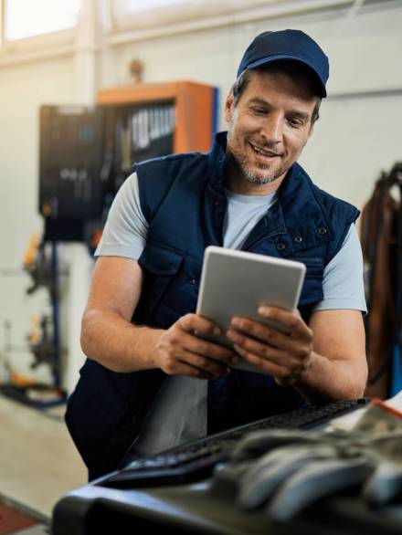 Happy car mechanic using digital tablet while working in auto repair shop.